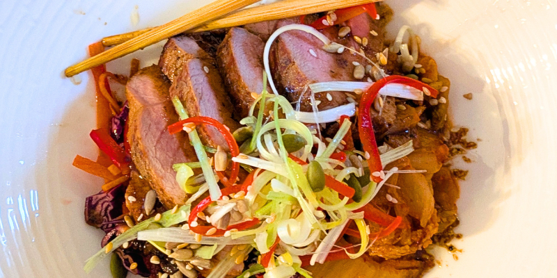 A white bowl filled with slices of pan-roast St Pirans pork, Cultura Kimchi Asian slaw and a raw Cornish honey sesame and soy dressing.